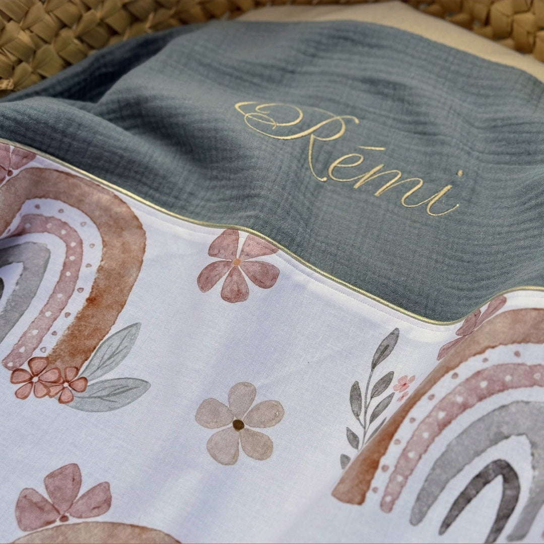 Detail van babydeken met beige-grijze regenboogprint en saliegroene achterkant met naam.