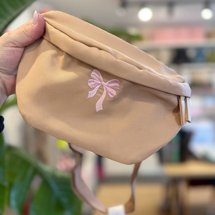 Close-up van een beige heuptas met een roze geborduurde strik.