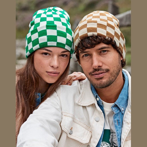 Twee personen dragen gebreide schaakbordmutsen in groen met ecru en beige met bruin.