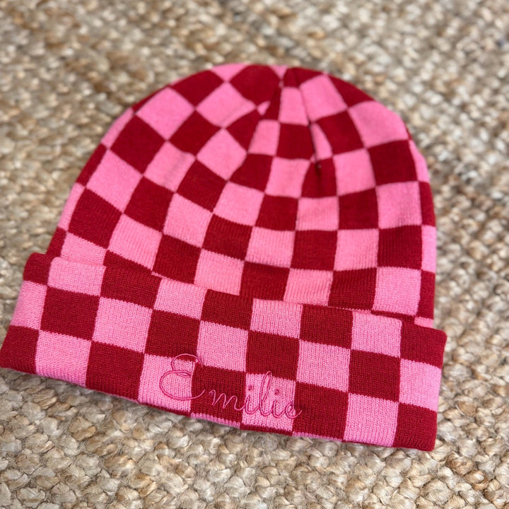 Roze en bordeaux gebreide schaakbordmuts met een geborduurde naam op de omslag.