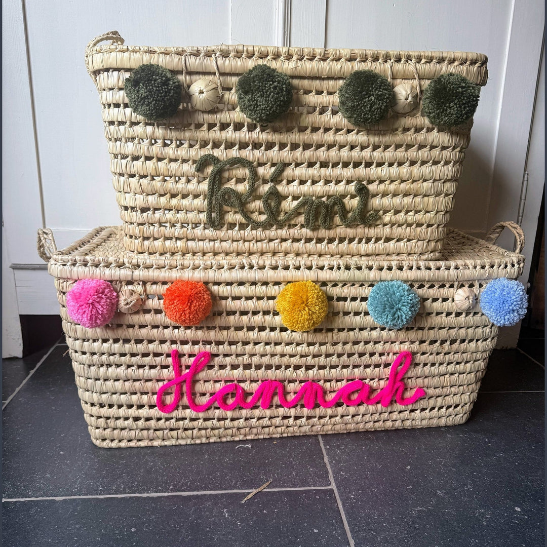 Natuurlijke palmbladmand met blauwe punnikletters en decoratieve pompons.