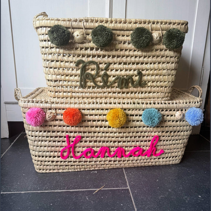 Natuurlijke palmbladmand met blauwe punnikletters en decoratieve pompons.