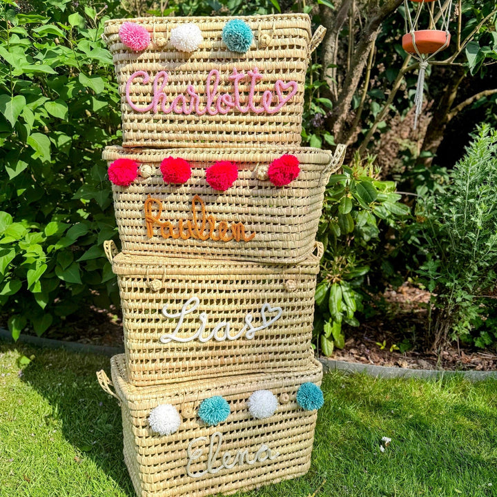 Palmbladmand met roze pompons, gefotografeerd buiten op een stenen pad.