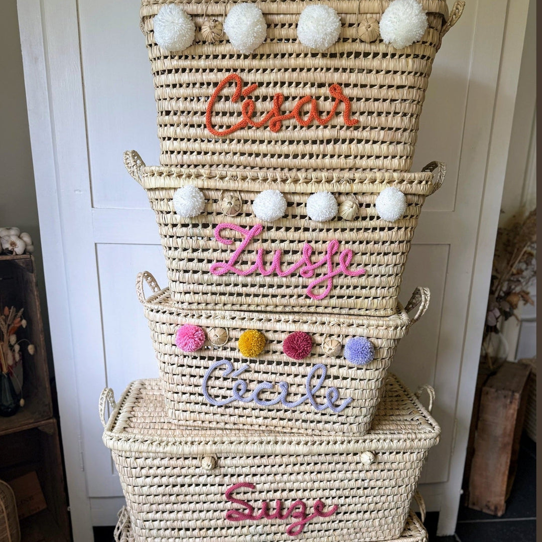 Palmbladmand met gekleurde punniknaam en pompons, gefotografeerd in de winkel.