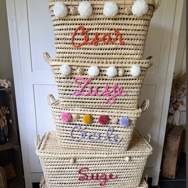 Palmbladmand met gekleurde punniknaam en pompons, gefotografeerd in de winkel.