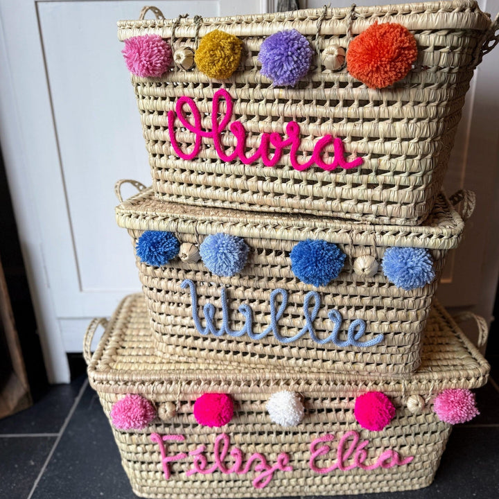 Verschillende palmbladmanden met kleurrijke punniknamen en pompons naast elkaar.