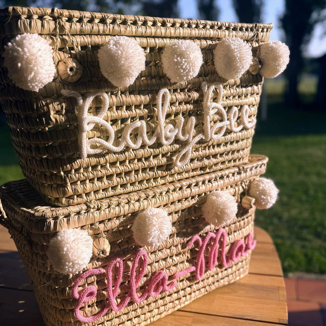 Twee handgemaakte palmbladmanden met verschillende punnikletters en pompons.