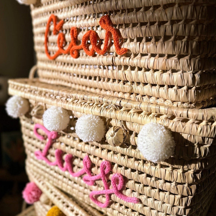 Palmbladmand met roze punnikletters en pompons aan de bovenrand.